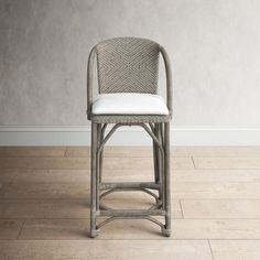 a gray wicker bar stool with white leather seat padding on a wood floor