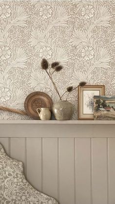 a shelf with pictures, vases and other items on it in front of a wallpapered background