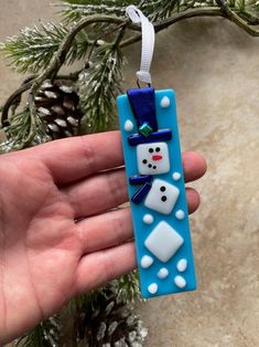 a hand holding a snowman ornament on top of a christmas tree branch