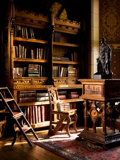 an old fashioned desk and chair in front of bookshelves with statues on them