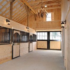 the inside of a horse barn with wooden stalls and chandeliers hanging from the ceiling