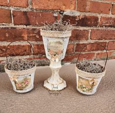 three white vases with plants in them sitting next to a brick wall