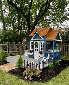 a small blue and white garden shed in the middle of a yard with flowers around it