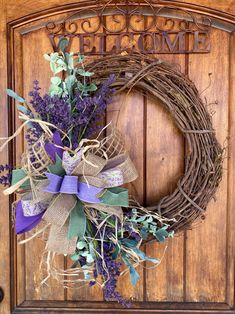 a wreath with purple flowers and green leaves is hanging on the front door to welcome guests