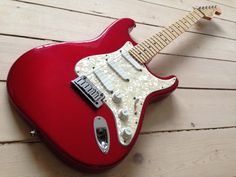 a red electric guitar sitting on top of a wooden floor next to a white wall