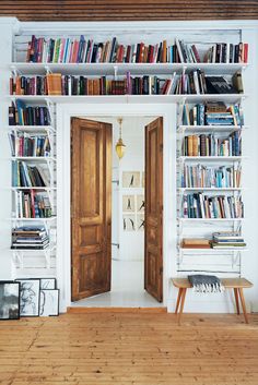 a bookshelf filled with lots of books next to two wooden doors in a room