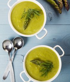 two bowls filled with green soup next to asparagus