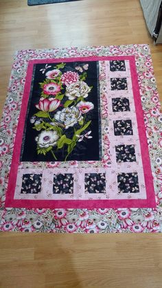 a black and pink rug with flowers on it in the middle of a wooden floor