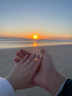 two people are holding hands on the beach as the sun is setting in the background