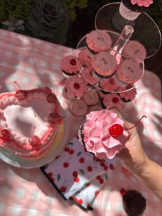 a person holding up a cupcake with pink frosting and cherries on it