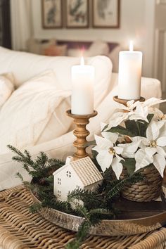 two white candles sitting on top of a wicker tray next to a christmas decoration