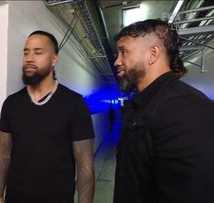 two men standing next to each other in front of a white wall with blue lights