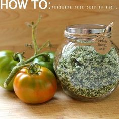 a jar filled with green and red stuff next to a tomato on a wooden table