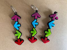 three pairs of earrings with different colored arrows hanging from hooks on a white table top