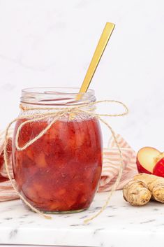 a jar filled with red liquid next to sliced apples and cinnamons on a marble surface