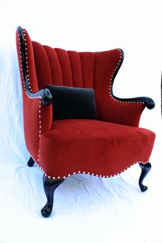 a red chair with studded trim and black pillow on it's back, against a white background