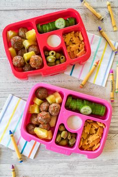 two plastic trays filled with food on top of a wooden table next to colored pencils