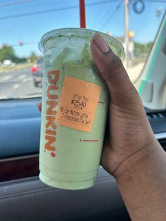 a hand holding up a drink in front of a car window with an orange sticker on it