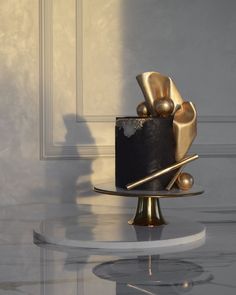 a black and gold cake on a white table with a shadow from the wall behind it