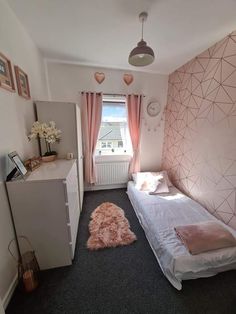 a bedroom with a bed, desk and dresser in it's corner area that has pink curtains on the windowsill