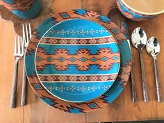 a place setting with blue and orange plates, silverware and utensils on a wooden table