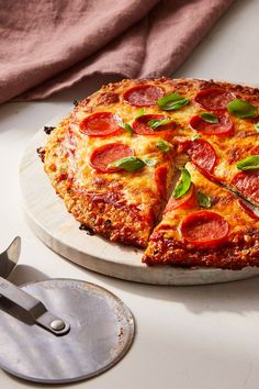 a pizza with pepperoni and basil on a white plate next to a spatula