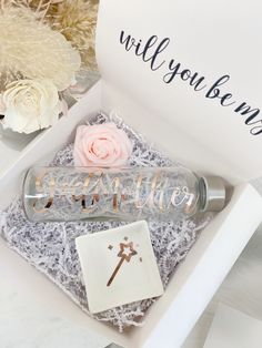 a glass bottle with a rose in it next to a card that says will you be my godmoter?