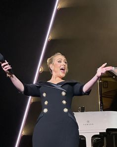 a woman in a black dress singing on stage with her hands out to the side