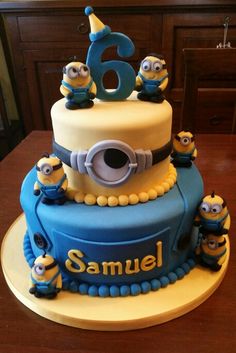 a blue and yellow birthday cake with minion figures on it's top tier