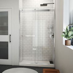 a white bathroom with a walk in shower next to a door and rug on the floor