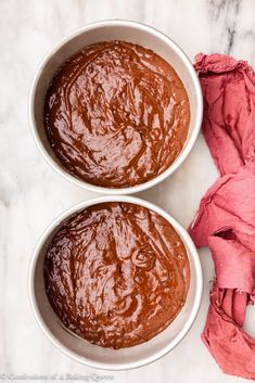 two white bowls filled with brown sauce on top of a marble counter next to pink napkins