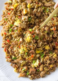 someone holding a wooden spoon over a plate of rice with meat and veggies