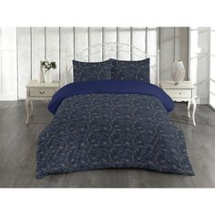 a bed with blue comforters and pillows in a white room next to a night stand