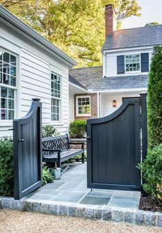 an open gate in front of a house with a bench and bushes on the side