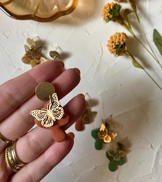 a hand holding a small gold butterfly on it's finger next to some flowers