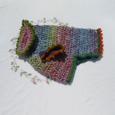 a multicolored knitted scarf laying on top of a white surface with flowers