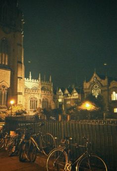 several bicycles are parked in front of a fence and building at night with lights on