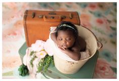 a baby is curled up in a bucket with flowers on the table next to it