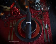 a red table cloth with black plates and silverware on it, next to candles