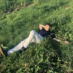 a man laying in the grass with his arms behind his head and eyes closed, resting