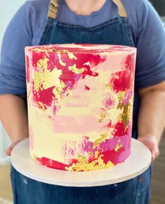 a person holding a cake with pink and yellow frosting