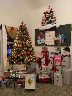 a christmas tree with presents under it in front of a wall decorated with gifts and santa hats