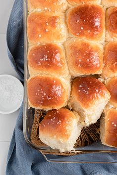 a baking dish filled with bread rolls on top of a blue towel next to a cup of milk