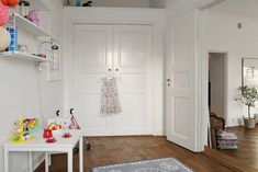 a room with white walls and wooden floors has a rug on the floor, two shelves holding toys