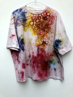 a t - shirt that has been dyed with different colors and designs on it, sitting on a hanger