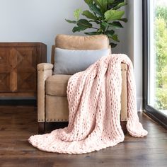 a chair with a blanket on it next to a plant in a room that has wooden floors