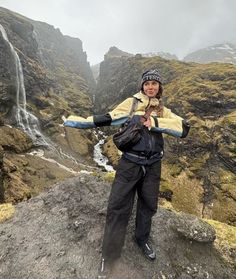 a woman standing on top of a rock next to a waterfall in the middle of nowhere