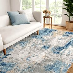 a living room with a white couch, blue rug and potted plant on the floor