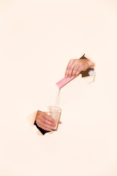 two hands holding toothbrushes over a cup filled with liquid and paper on white background