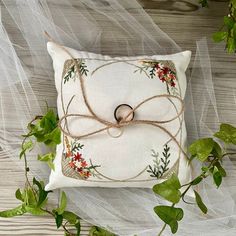 a white pillow with a ring on it surrounded by green leaves and vines, sitting on a wooden surface